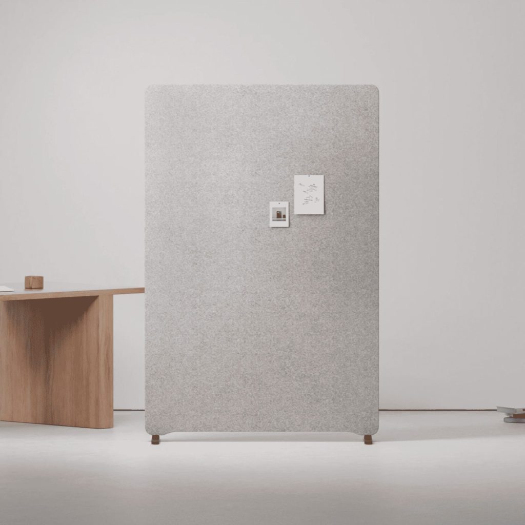 Panneau acoustique en feutre gris clair posé contre un mur, près d’un bureau en bois