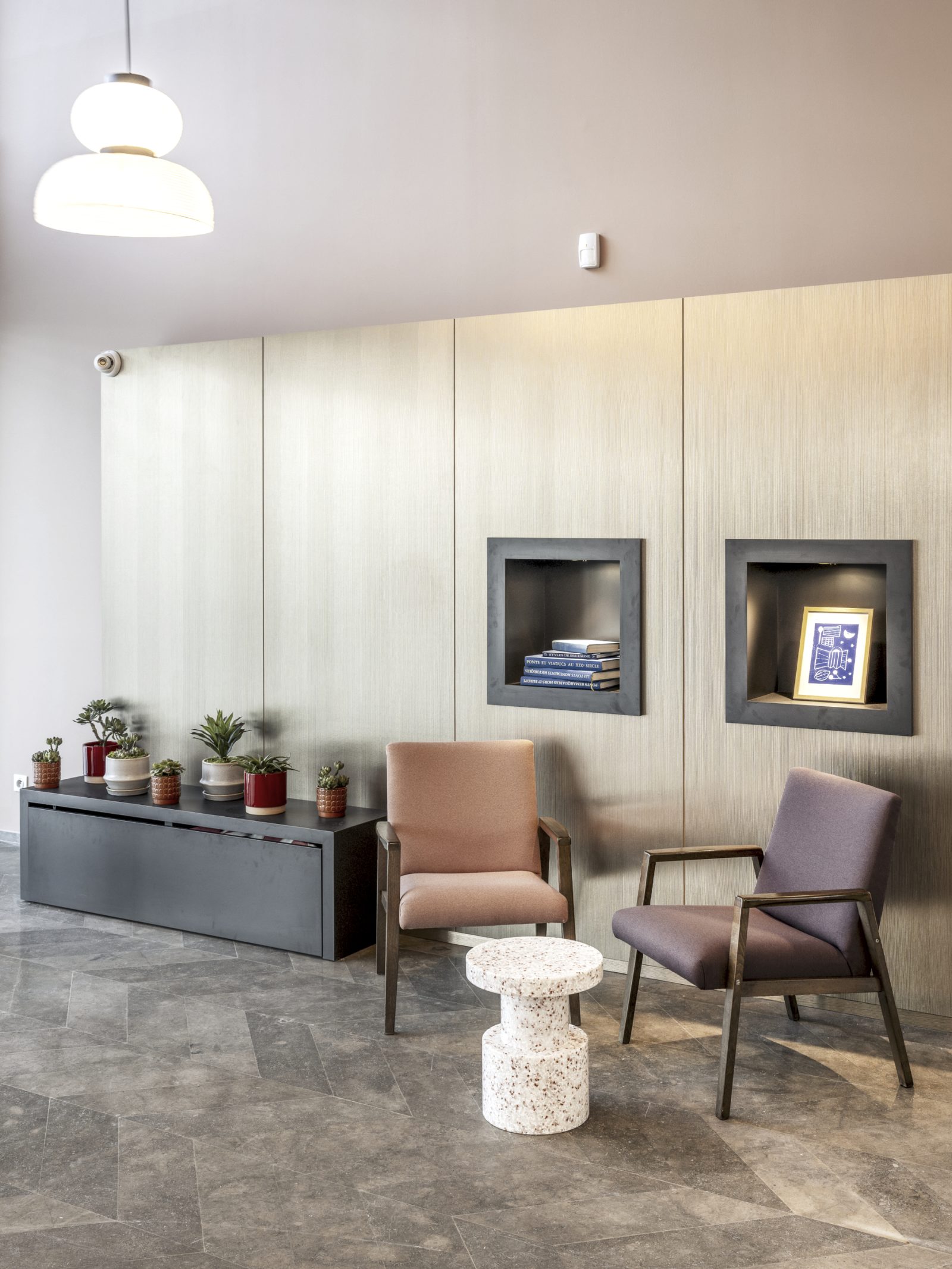 Espace d’accueil avec deux fauteuils, une table d’appoint en terrazzo et des niches murales