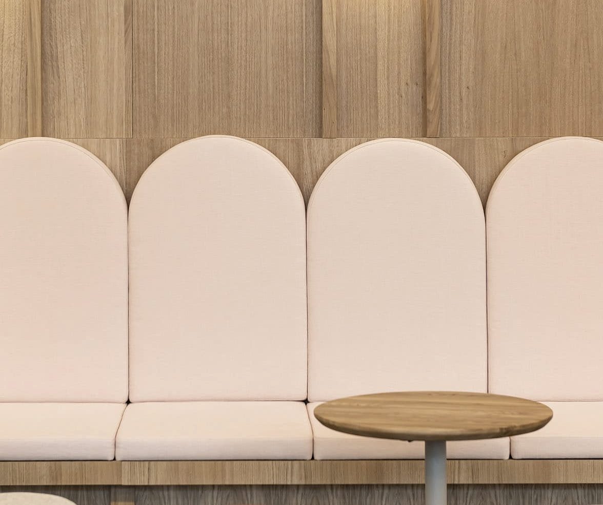 Banquette à dossiers arrondis et table ronde en bois devant un mur en panneaux de bois